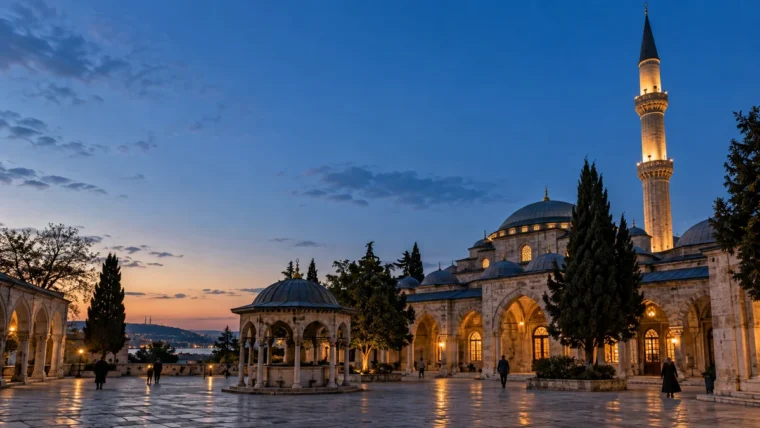Alacakaranlıkta ışıkları yanan tarihi cami avlusu, minare ve uzakta yürüyen yetişkinler